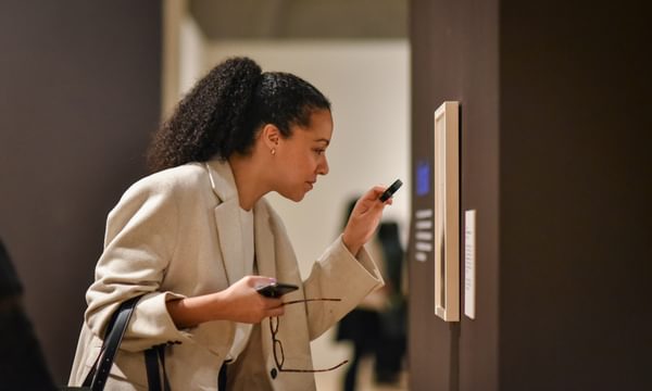 Side view of a lady with a magnifying glass looking at an artwork on display.