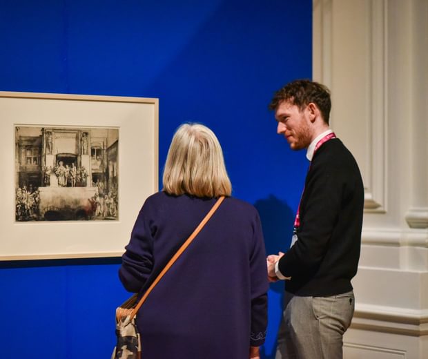 A visitor talking to a member of staff in front of an artwork on display.