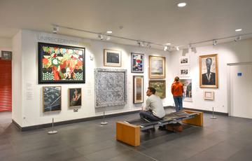 Two visitors in an exhibition space with a variety of modern paintings and artworks on the walls