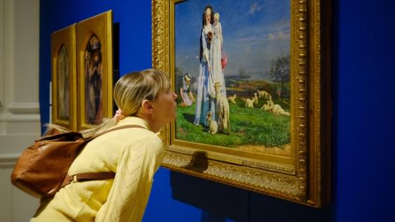 A lady is leaning in to take a closer look at a painting the Pretty Baa Lambs.
