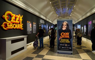 Ozzy Osbourne exhibition with large 'Ozzy Osbourne' graphic, black walls and people in the exhibition space.