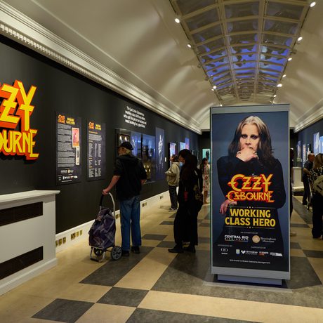 Ozzy Osbourne exhibition with large 'Ozzy Osbourne' graphic, black walls and people in the exhibition space.