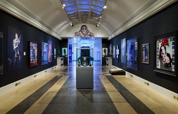 An end view of the Bridge Gallery with objects and artworks on the walls and display case of awards in the centre.
