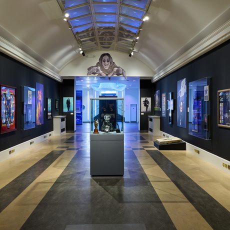 An end view of the Bridge Gallery with objects and artworks on the walls and display case of awards in the centre.