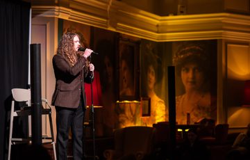 Bradley Taylor on stage, in the background are large portraits and warm lighting.