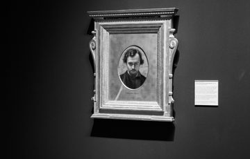 Black and white portrait of a man in an ornate rectangular frame on dark wall.
