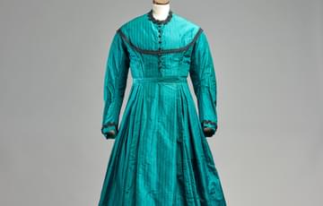An Victorian emerald green dress with a thin black trimming on collar and cuffs and neck.