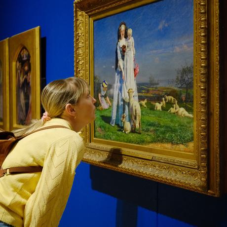A lady is leaning in to take a closer look at a painting the Pretty Baa Lambs.