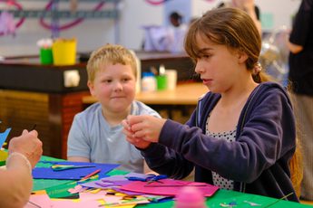 Two children engaged in crafting with colourful paper and scissors at a table.