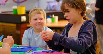 Two children engaged in crafting with colourful paper and scissors at a table.