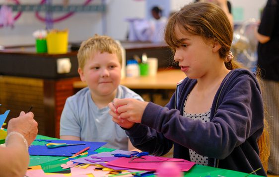 Two children engaged in crafting with colourful paper and scissors at a table.