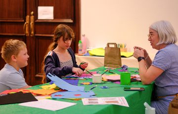 Two children and an adult engaged in arts and crafts at a table.