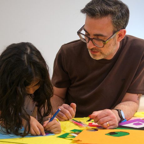 A man and girl focused on colourful paper crafts at a table together.