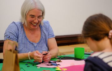 An woman and young girl happily crafting with colourful paper and scissors.