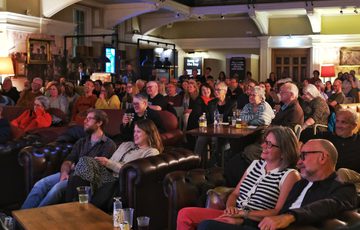 Audience attentively watching a performance or presentation in a cozy, dimly lit venue.
