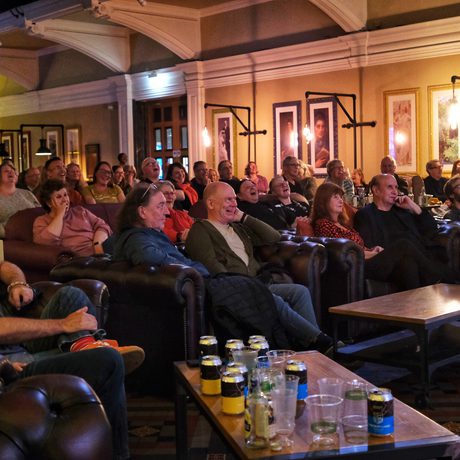Audience enjoying a comedy show or live performance in a cozy, warmly lit venue.