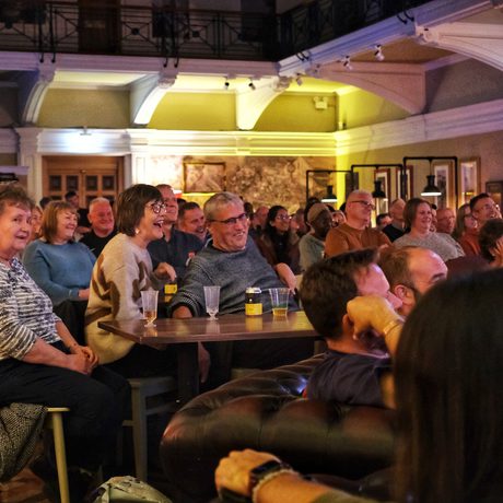 Audience seated at tables, enjoying a live performance in a cozy, warmly lit venue.