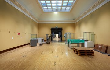 An empty gallery with pale yellow walls, and empty display cases.