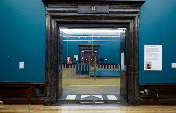 A ornate black doorway with glazed doors leading onto another gallery.
