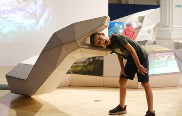 A large 3D model of an life size giant snake with a child putting their head inside and looking surprised.