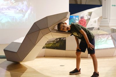 A large 3D model of an life size giant snake with a child putting their head inside and looking surprised.