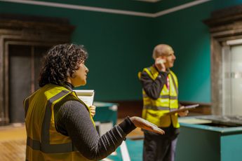 A staff member in a high vis vest with another staff member behind, an empty gallery is behind them.