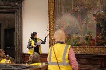 A staff member pointing to a large waiting on display and giving a tour to a group of people wearing high vis vests.