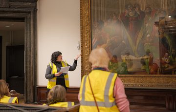 A staff member pointing to a large waiting on display and giving a tour to a group of people wearing high vis vests.