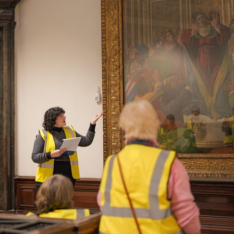 A staff member pointing to a large waiting on display and giving a tour to a group of people wearing high vis vests.
