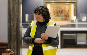 A staff member in a high vis jacket smiling in a gallery doorway.