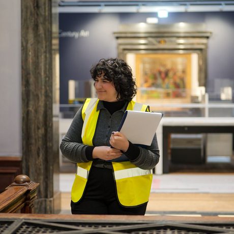 A staff member in a high vis jacket smiling in a gallery doorway.