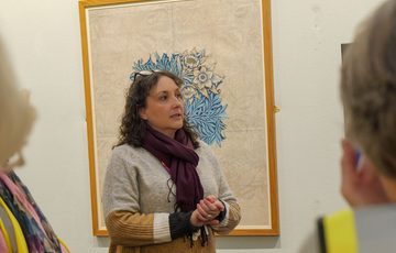 A staff member facing two two people with their backs to the camera. An artwork is on display behind the staff member.
