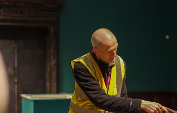 A staff member in a high vis vest pointing to something out of shot.