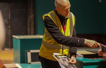 A staff member in a high vis vest pointing to something out of shot.