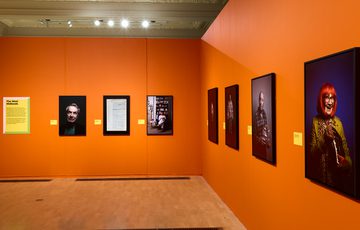 Portraits photographs showcased on bright orange walls in a modern art gallery setting.