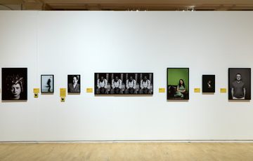 Portraits photos of various comedians displayed on a white gallery wall.