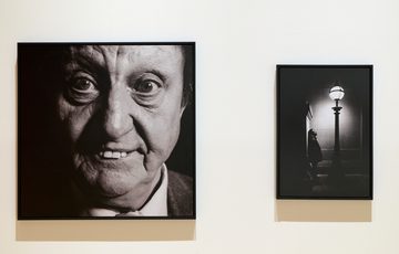 Two framed black-and-white photos: close-up portrait photograph of Ken Dodd and shadowy figure of Romesh Ranganathan by streetlamp.