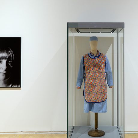 Black-and-white portrait of Victoria Wood contrasts with colourful patterned 'Dinnerladies' dress displayed in glass case.