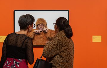 Two women closely observing a framed photograph Bill Oddie in a furry animal costume.