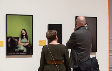 Two people viewing framed photographs displayed on a gallery wall.