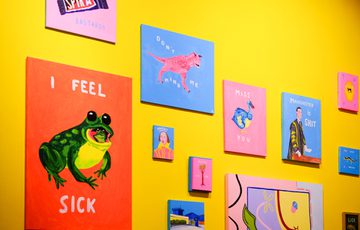 Colourful paintings with texts displayed on a bright yellow wall.