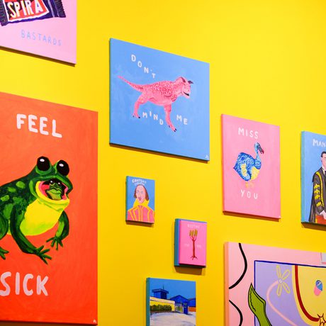 Colourful paintings with texts displayed on a bright yellow wall.