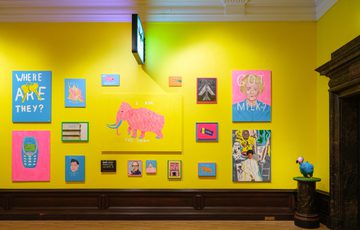 Bright yellow wall adorned with colourful artworks and a dodo statue on pedestal.