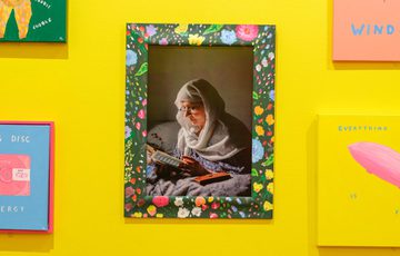 Colourful artworks surround a central floral-framed photo of a woman reading.