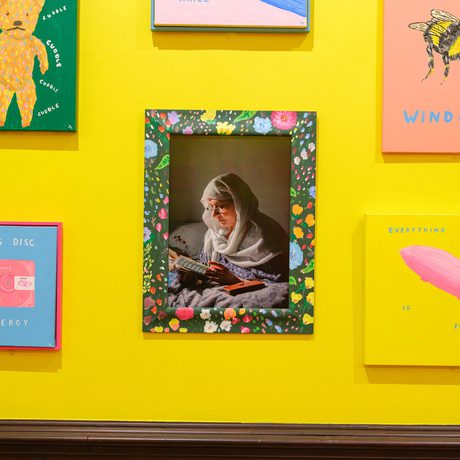 Colourful artworks surround a central floral-framed photo of a woman reading.