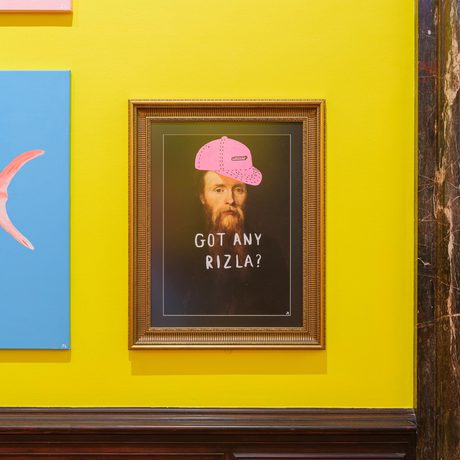 Framed portrait of a bearded man wearing a pink cap with "GOT ANY RIZLA?" text.