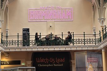 Lots of people in a gallery looking at a string quartet playing on the balcony above.