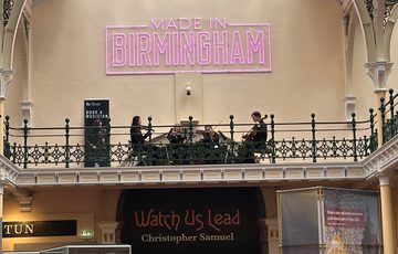 Lots of people in a gallery looking at a string quartet playing on the balcony above.