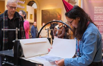 A person examines a print on an old printing press in a museum.