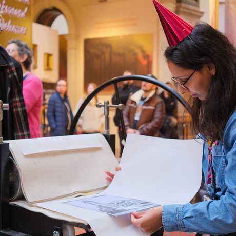 A person examines a print on an old printing press in a museum.